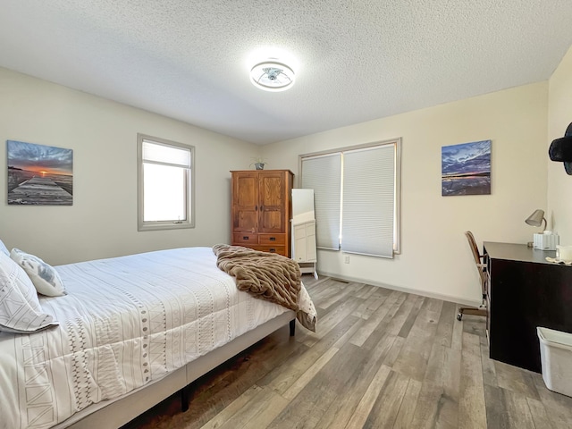 bedroom with a textured ceiling, baseboards, and light wood-style floors