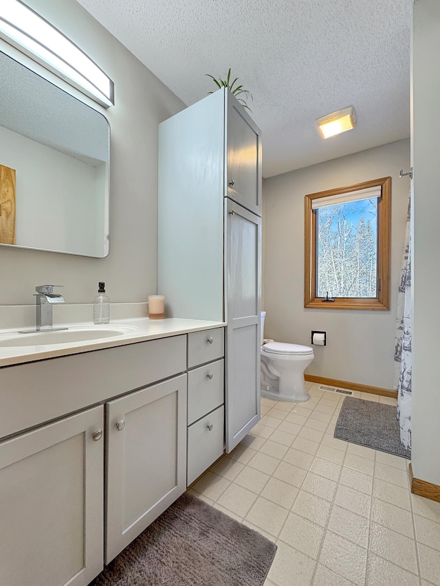 bathroom with a textured ceiling, vanity, toilet, and baseboards