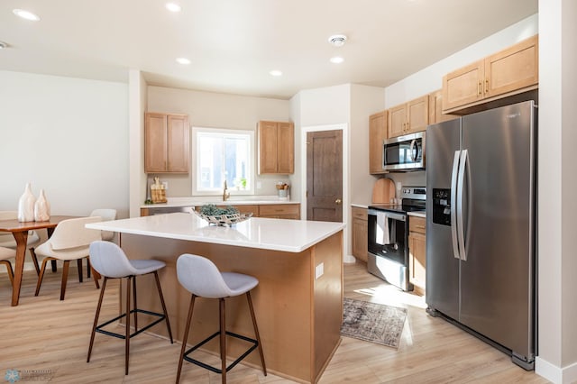 kitchen with a kitchen island, a kitchen breakfast bar, appliances with stainless steel finishes, light wood-type flooring, and light brown cabinetry