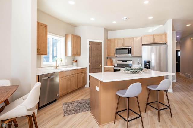 kitchen with light wood-style flooring, appliances with stainless steel finishes, a center island, a kitchen bar, and a sink