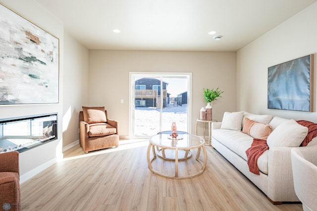 living area with a glass covered fireplace, recessed lighting, wood finished floors, and baseboards