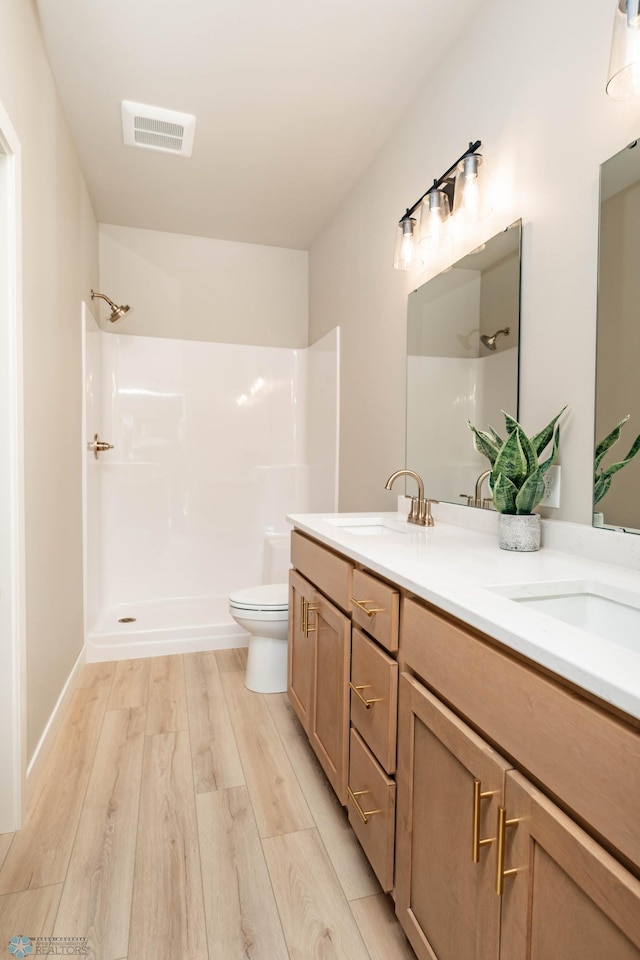 bathroom featuring visible vents, a shower, a sink, and wood finished floors