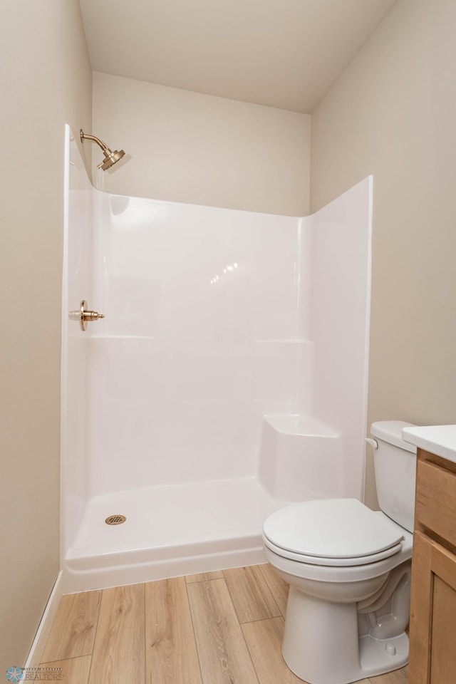 bathroom featuring a shower, vanity, wood finished floors, and toilet