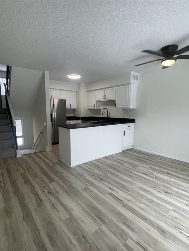 kitchen featuring dark countertops, stainless steel fridge, a peninsula, white cabinets, and light wood finished floors