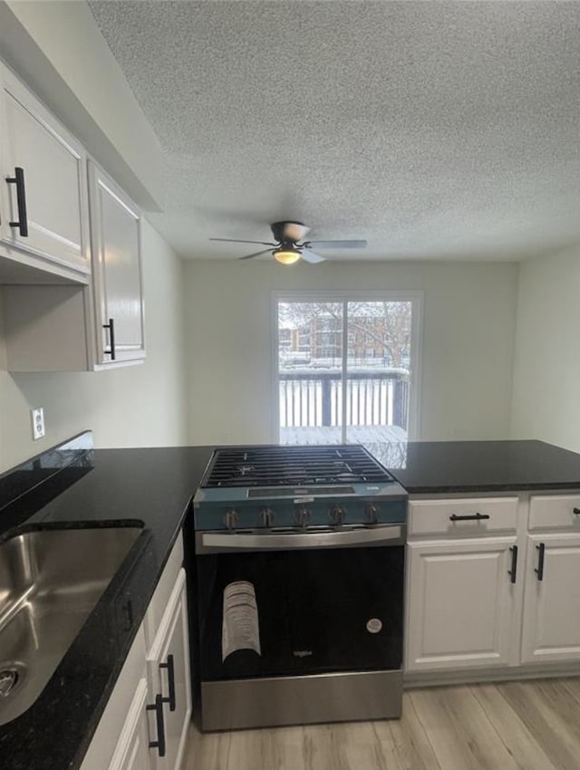 kitchen featuring dark countertops, gas range, light wood-style floors, white cabinets, and a sink