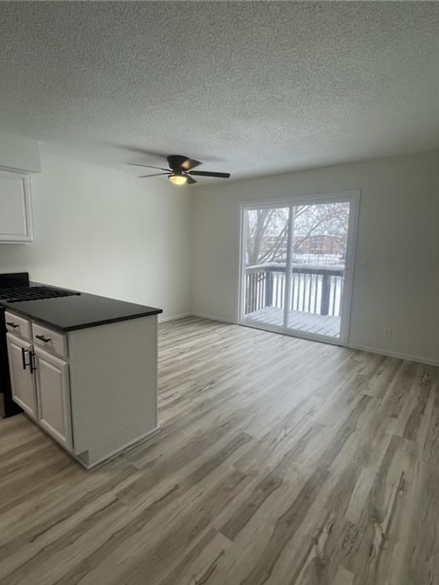 unfurnished living room featuring light wood-type flooring, baseboards, a textured ceiling, and a ceiling fan