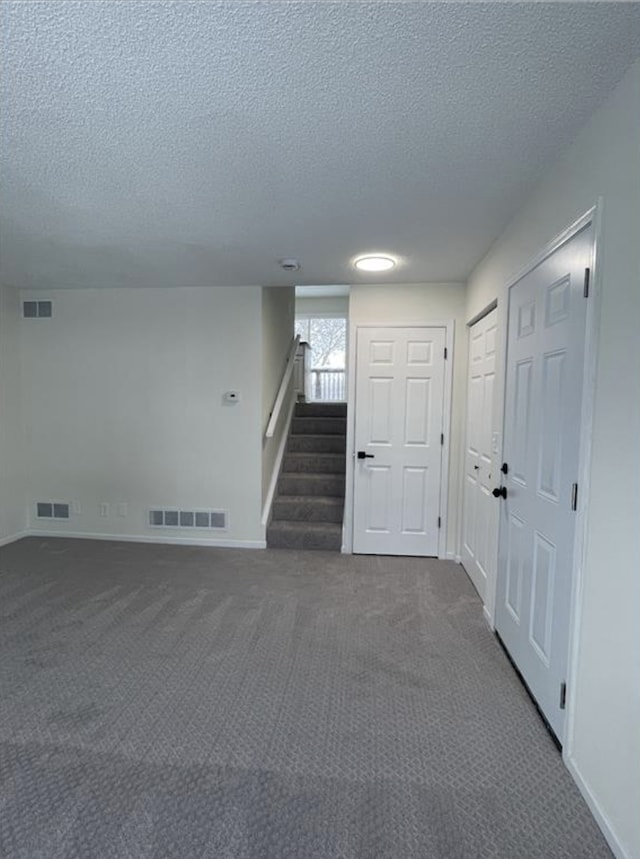 interior space with dark colored carpet, visible vents, and stairway