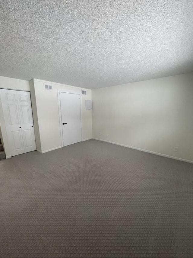 unfurnished bedroom with visible vents, dark carpet, a textured ceiling, and baseboards