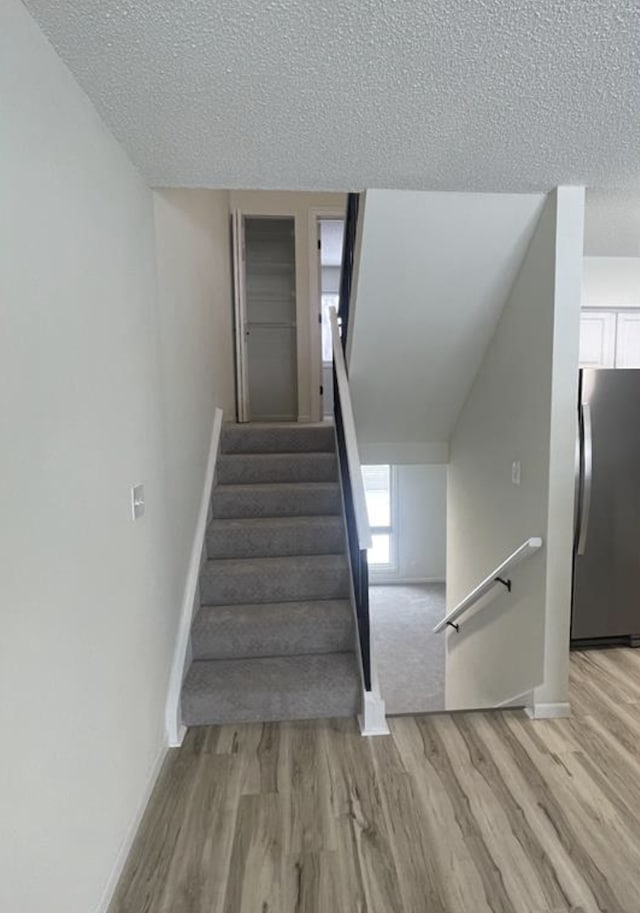 stairway featuring wood finished floors, baseboards, and a textured ceiling