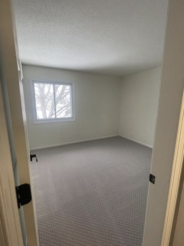 carpeted spare room featuring a textured ceiling and baseboards