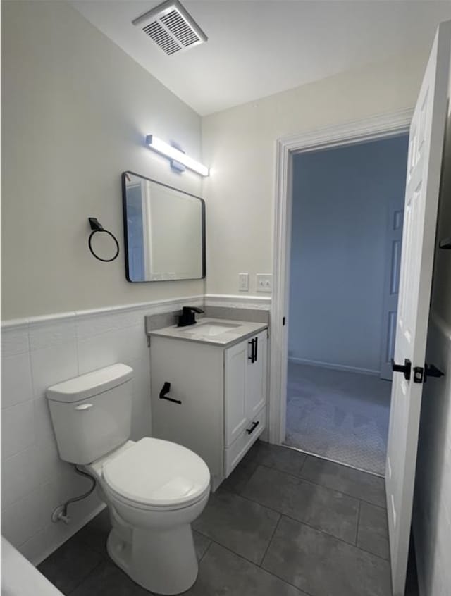 half bath with tile patterned floors, visible vents, wainscoting, and vanity