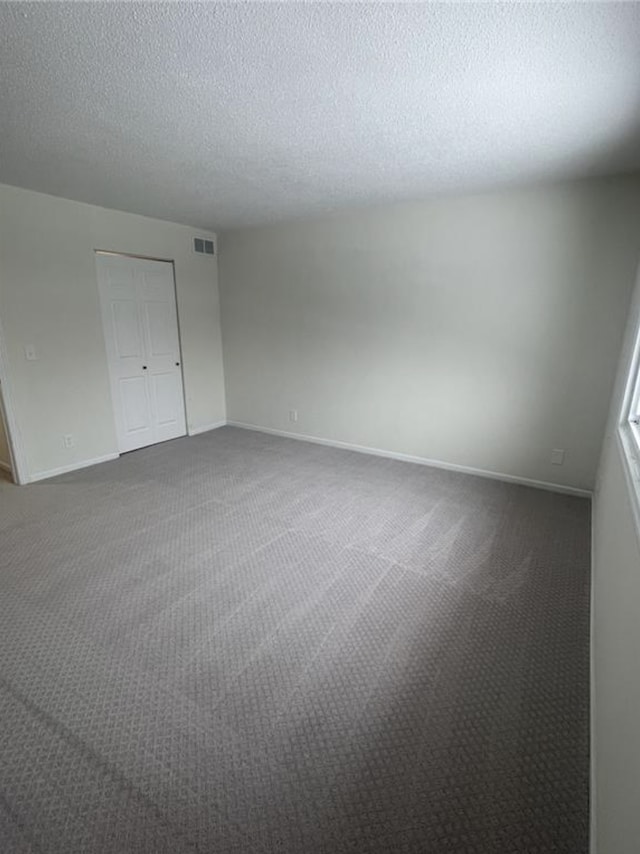 spare room featuring baseboards, visible vents, dark carpet, and a textured ceiling