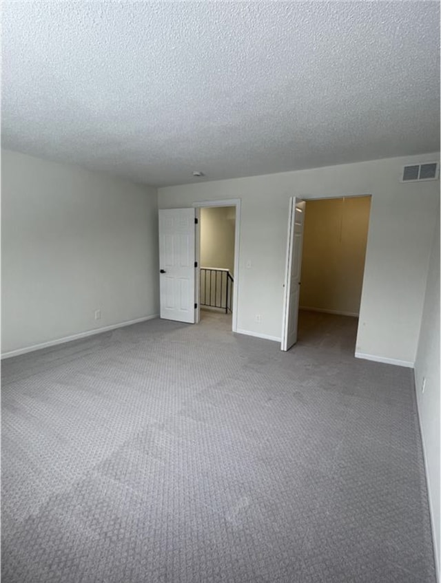 carpeted spare room with baseboards, visible vents, and a textured ceiling