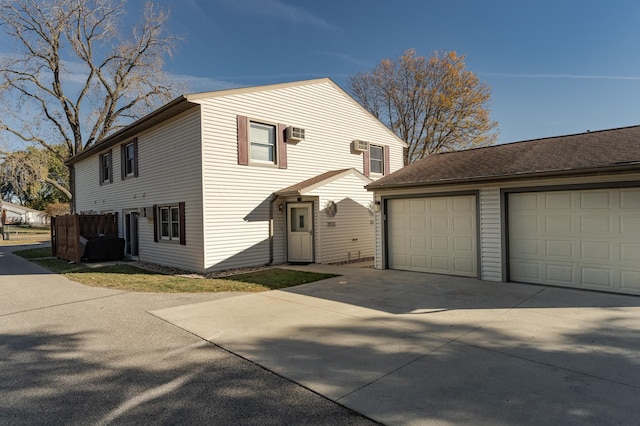 exterior space with a garage, an AC wall unit, and an outbuilding