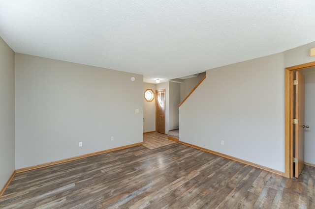 spare room featuring a textured ceiling, stairway, wood finished floors, and baseboards