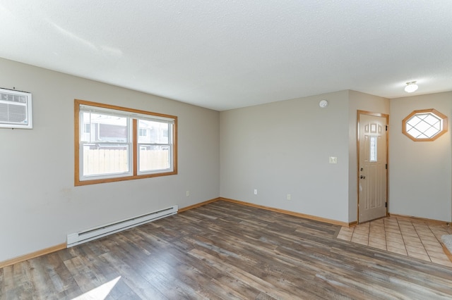 spare room featuring baseboards, wood finished floors, a wall mounted air conditioner, a textured ceiling, and a baseboard heating unit