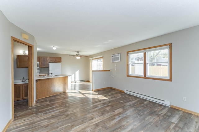 unfurnished living room with an AC wall unit, a baseboard radiator, wood finished floors, and baseboards