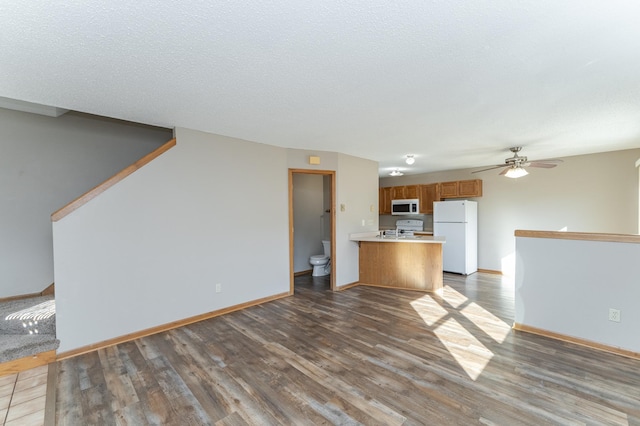 kitchen featuring white appliances, brown cabinetry, wood finished floors, a peninsula, and light countertops