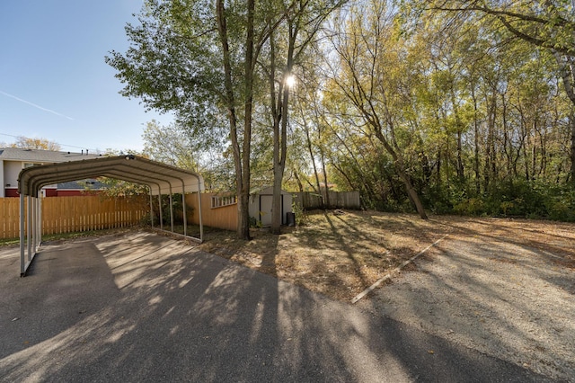 view of yard featuring aphalt driveway, a storage unit, fence, a carport, and an outdoor structure