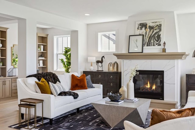 living area with a wealth of natural light, a high end fireplace, light wood-style flooring, and built in shelves