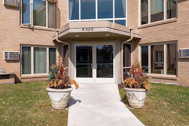 property entrance with a yard, french doors, an AC wall unit, and brick siding