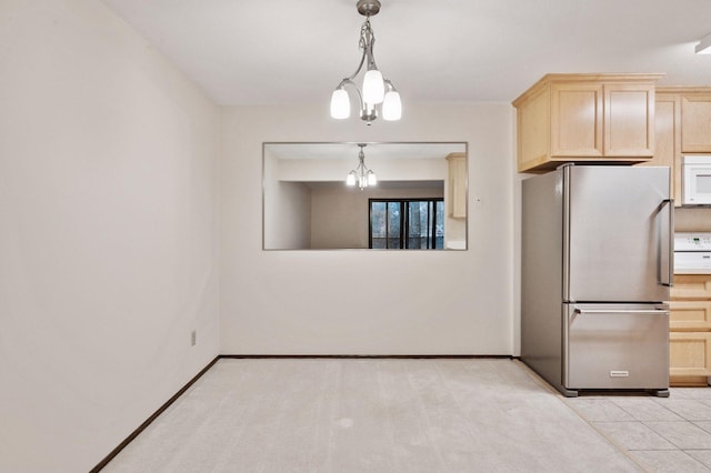 kitchen with a chandelier, white microwave, baseboards, freestanding refrigerator, and light brown cabinetry