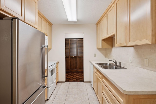 kitchen with white appliances, light countertops, a textured ceiling, light brown cabinets, and a sink