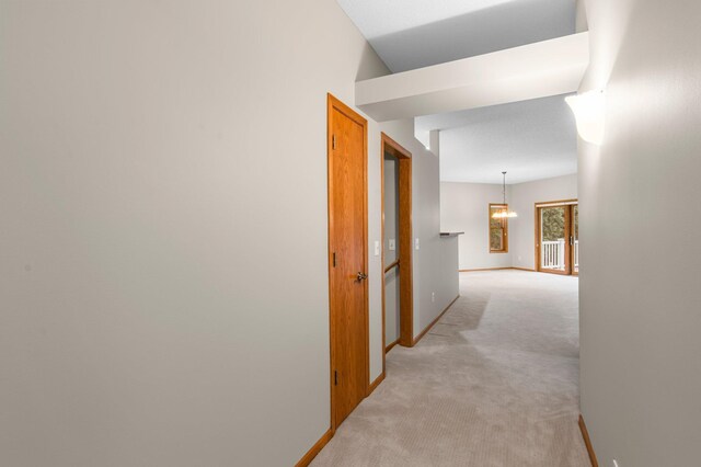 hallway with baseboards, an inviting chandelier, and light colored carpet