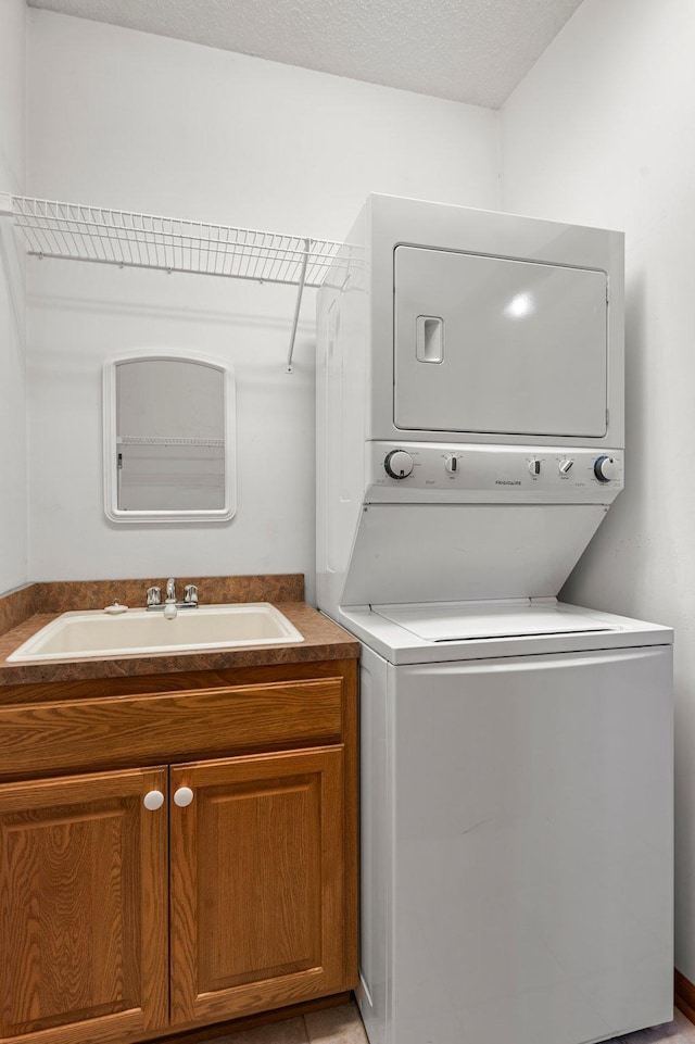 laundry room featuring a textured ceiling, cabinet space, a sink, and stacked washer and clothes dryer