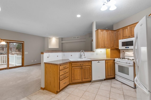 kitchen featuring a peninsula, white appliances, a sink, visible vents, and backsplash