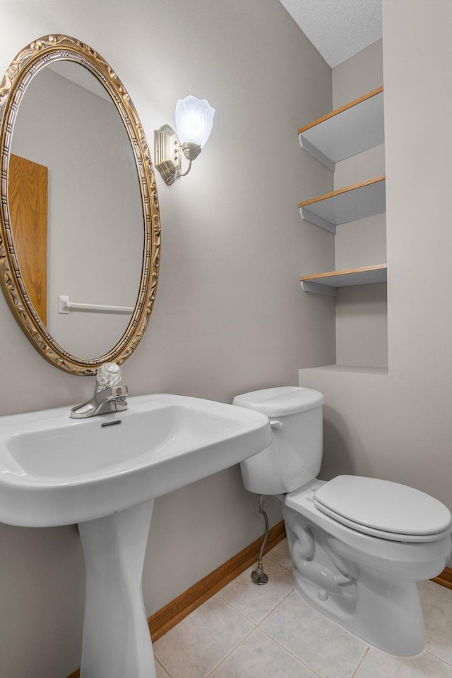 half bath with toilet, baseboards, a sink, and tile patterned floors