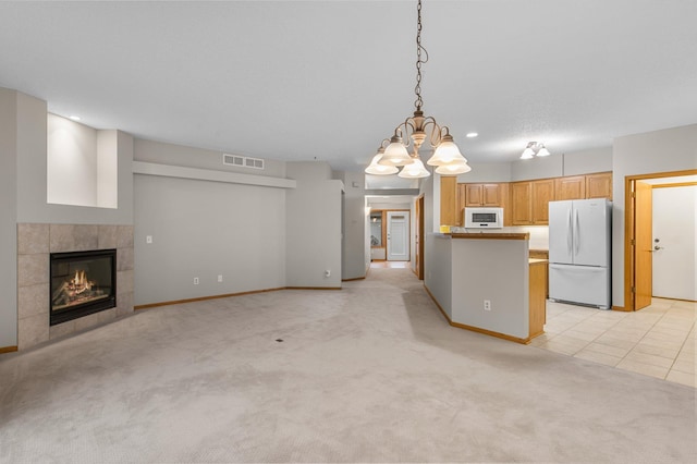 kitchen featuring white appliances, visible vents, a tiled fireplace, light colored carpet, and open floor plan