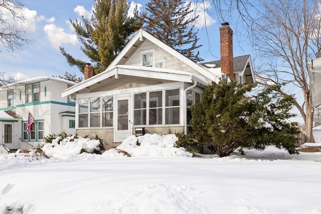 snow covered property featuring a sunroom and a chimney