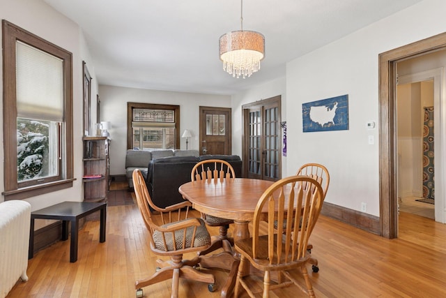 dining room with radiator, baseboards, light wood-type flooring, and an inviting chandelier