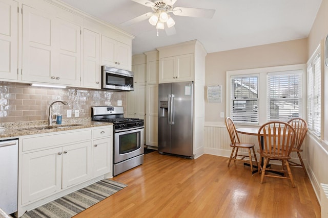 kitchen with backsplash, wainscoting, light wood-style floors, stainless steel appliances, and a sink