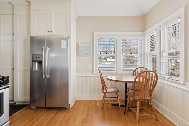 kitchen with a wealth of natural light, a wainscoted wall, stainless steel fridge, and light wood-style floors