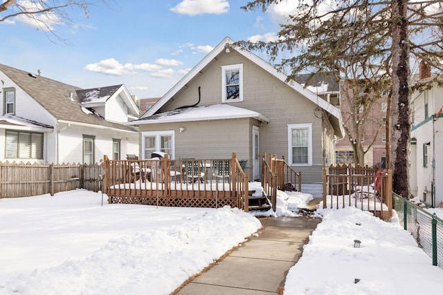 snow covered back of property with a deck and fence