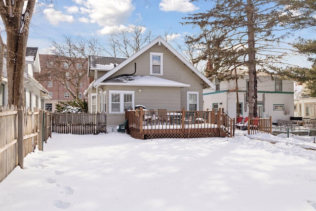 snow covered house with fence and a wooden deck