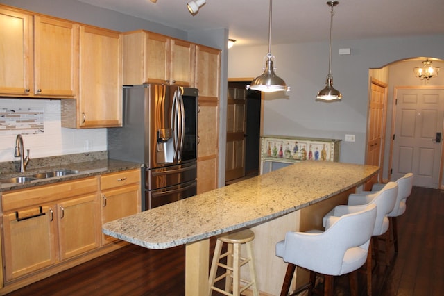 kitchen with dark wood-type flooring, stainless steel fridge with ice dispenser, arched walkways, and a sink