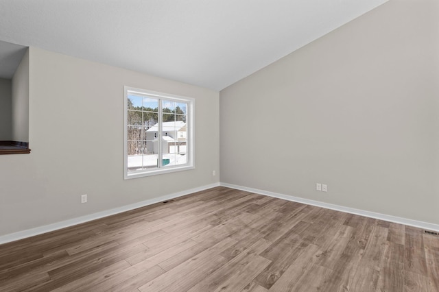 spare room featuring lofted ceiling, baseboards, and wood finished floors
