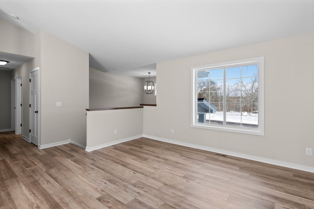 spare room with baseboards, an inviting chandelier, and wood finished floors