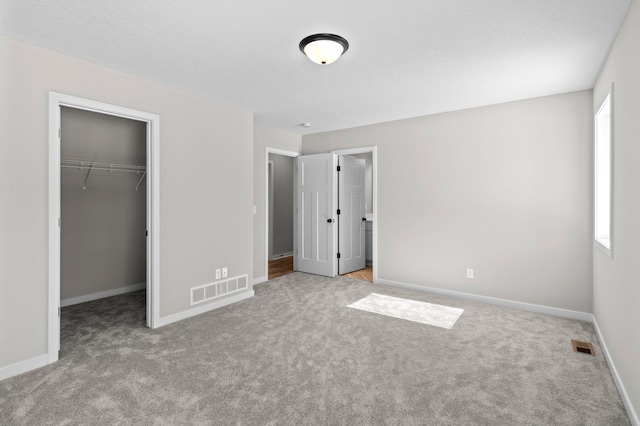 unfurnished bedroom featuring a walk in closet, baseboards, carpet, and visible vents