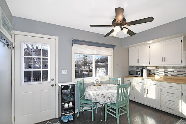 kitchen with stainless steel microwave, backsplash, light countertops, white cabinets, and dark wood-style flooring