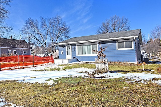 bungalow-style house with central air condition unit, fence, and a lawn