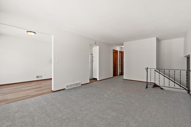 carpeted spare room with visible vents, a textured ceiling, and baseboards