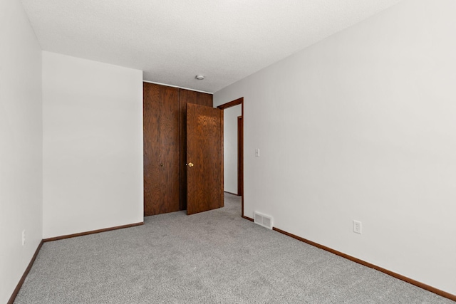 empty room with baseboards, visible vents, carpet floors, and a textured ceiling