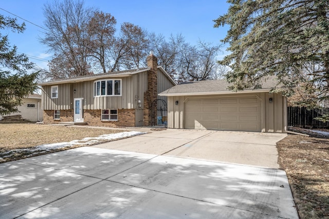 raised ranch with board and batten siding, concrete driveway, brick siding, and a chimney