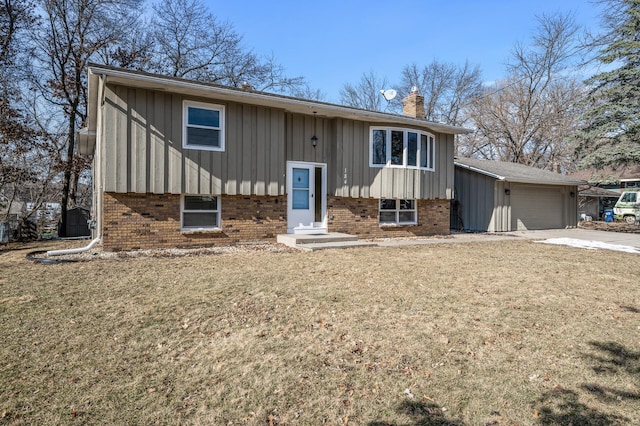 bi-level home with brick siding, a chimney, an attached garage, and a front lawn