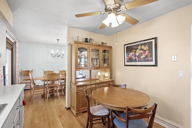 dining space with a textured ceiling, baseboard heating, ceiling fan with notable chandelier, and light wood-type flooring