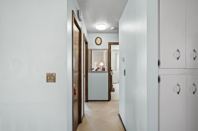 hallway featuring a textured ceiling, baseboards, and light colored carpet